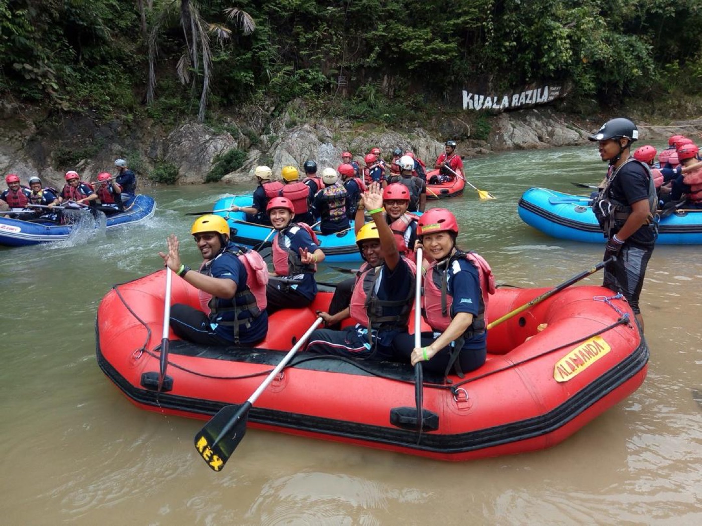 Corporate team waving from red raft on Sungai Kampar river during team building rafting activity